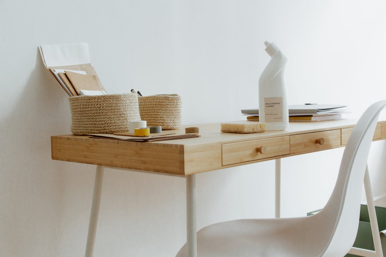 A clean and organized home office desk with cleaning products, papers, and storage baskets.